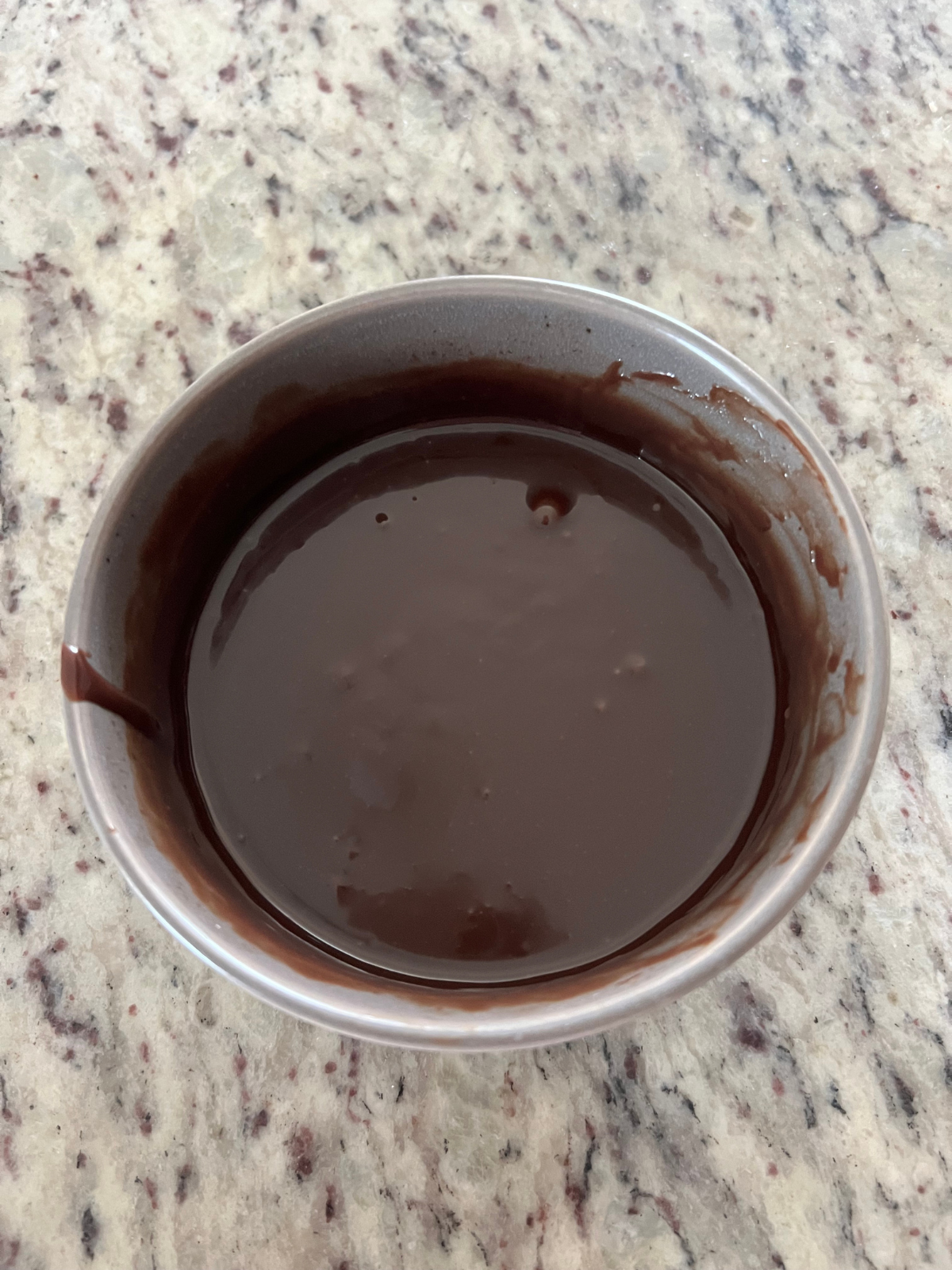 The chocolate ganache sits in a bowl ready to be poured over the sourdough brownie loaf.
