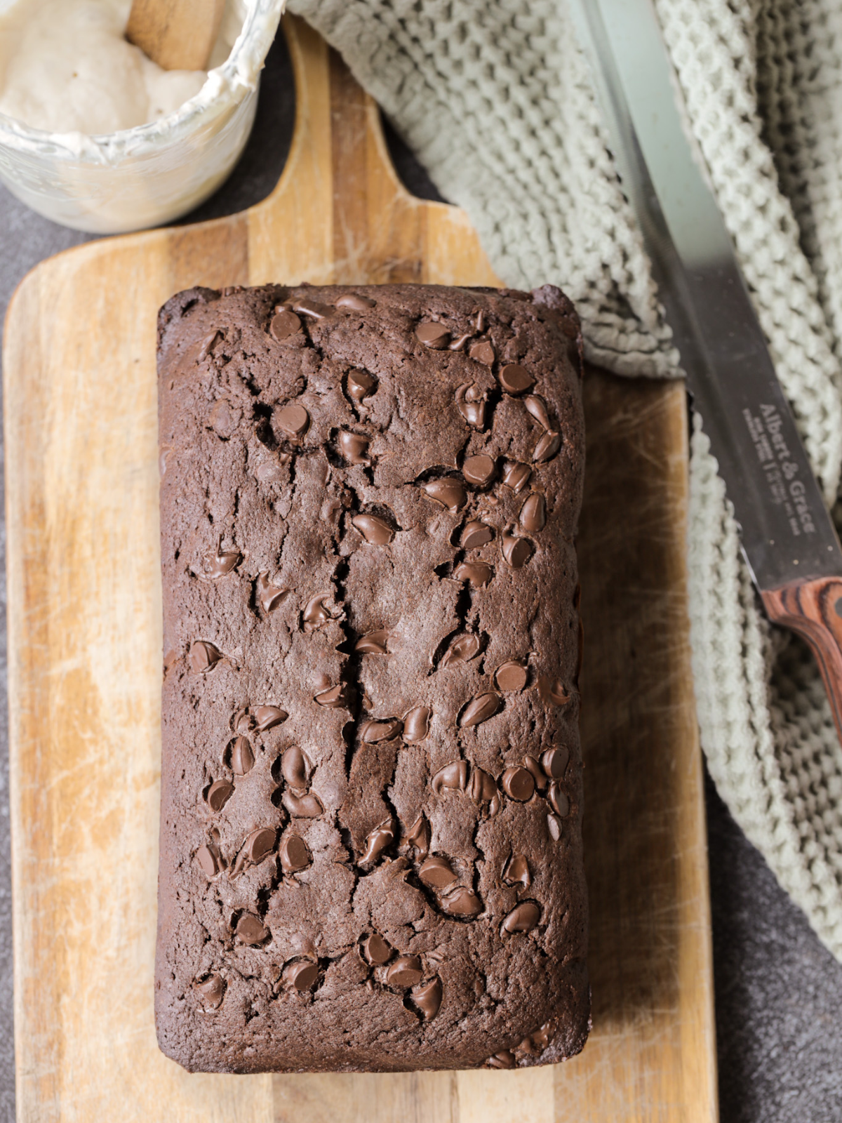 Freshly baked sourdough discard brownie bread is shown on a wooden cutting board before the chocolate ganache is poured over it.