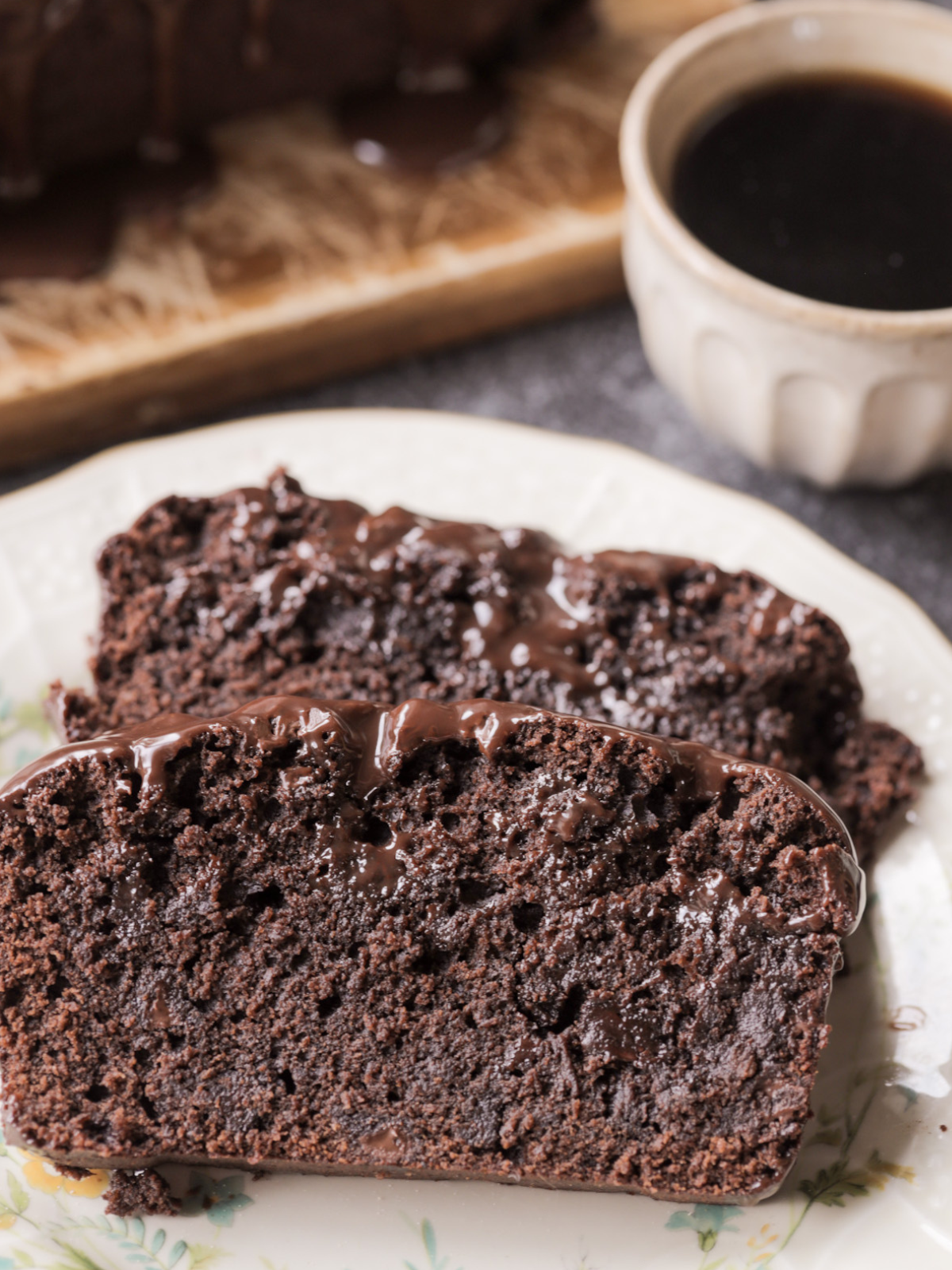 Sourdough discard chocolate fudgy brownie bread is shown with two slices cut out and sitting on a plate. A cup of coffee rests in the background.