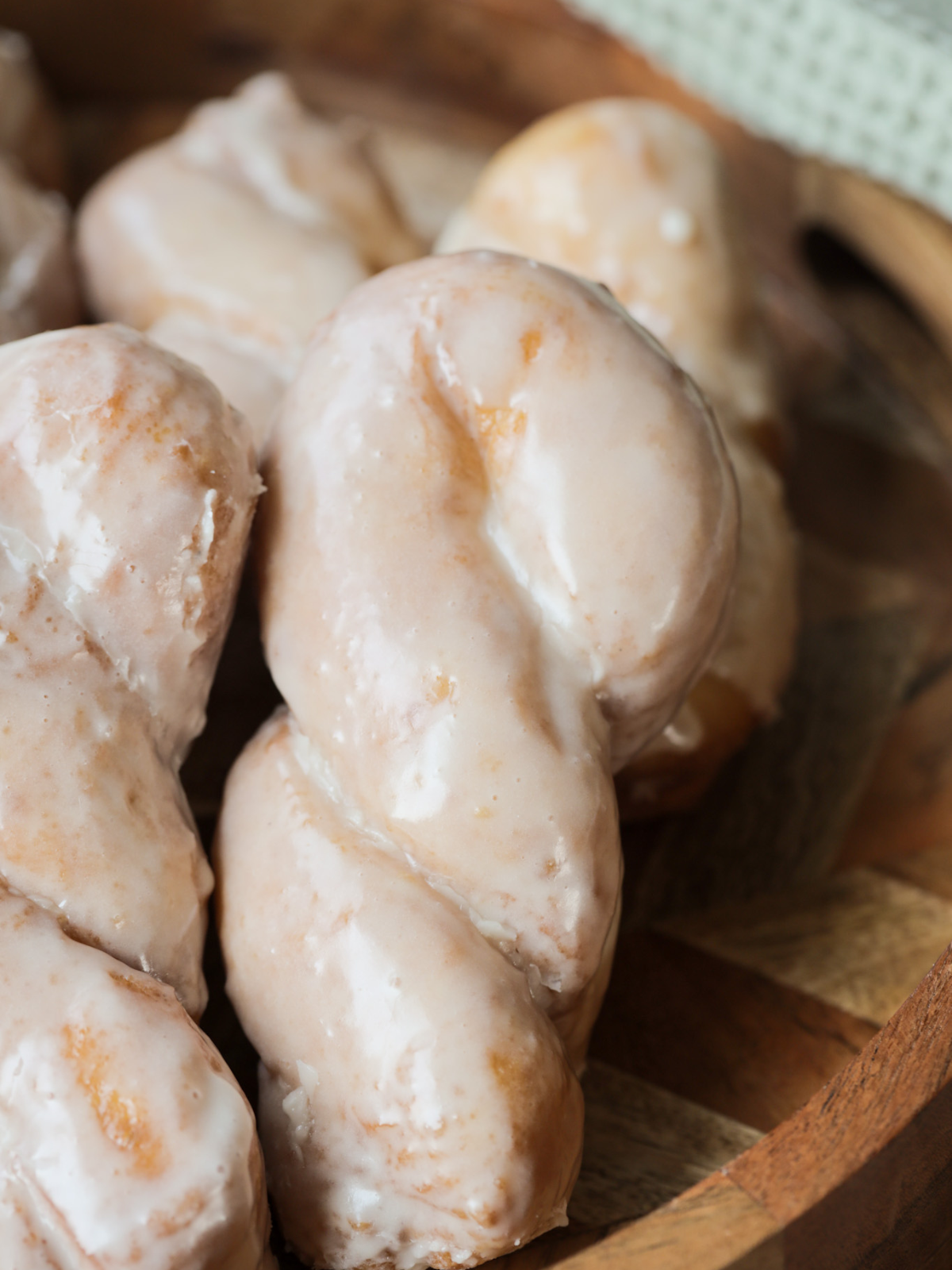 A closeup of a golden brown fried sourdough maple glazed donut with several others in the background.