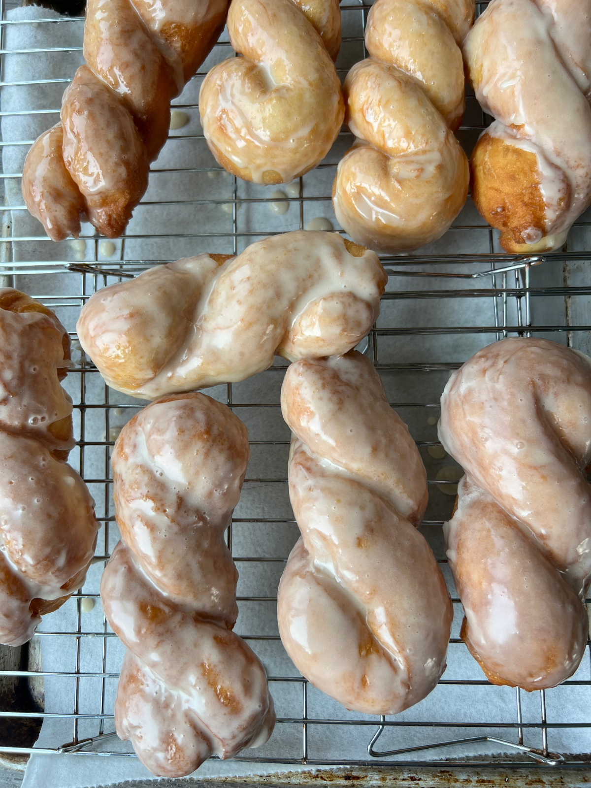 The sourdough maple twist donuts are shown on a wire rack setting after being dipped in maple glaze.