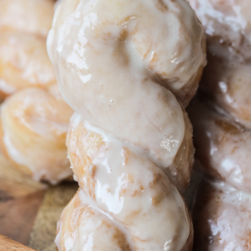 A closeup is shown of a sourdough brioche maple glazed twist donut with several others laying in the background.