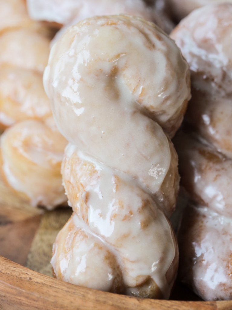 A closeup is shown of a sourdough brioche maple glazed twist donut with several others laying in the background.