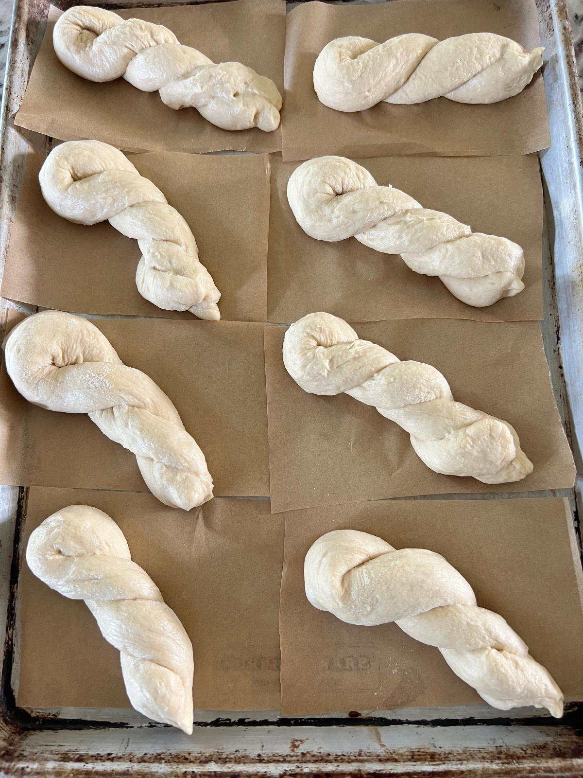 The sourdough twist donut dough pieces are shown shaped and sitting on individual parchment paper squares where they will have their second rise.