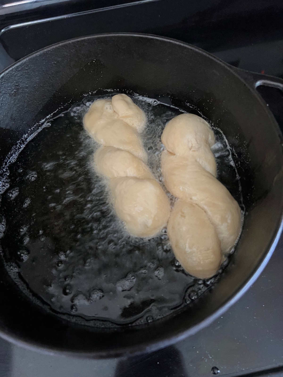 Two sourdough maple twist donuts are shown frying in the fryer oil.