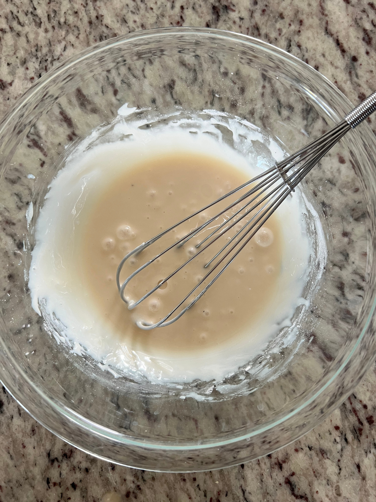 The maple glaze is shown in a glass mixing bowl with a whisk in it.