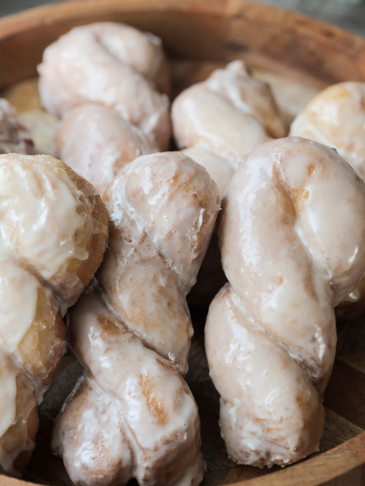 Several golden brown, fluffy sourdough maple glazed twist donuts rest on a wooden platter.