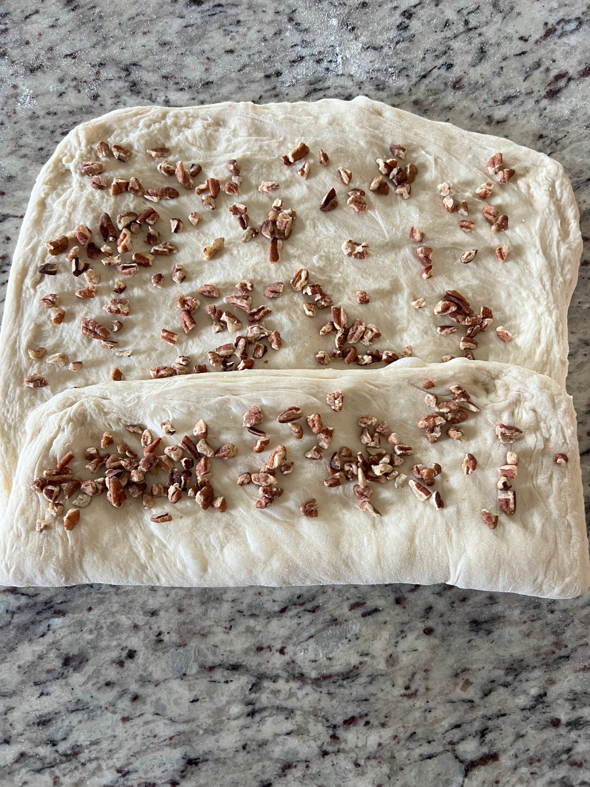 The dough for the sourdough pecan maple bread has been folded over a third of the rectangle and covered with chopped pecans.