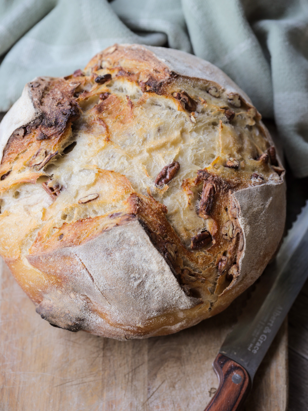 The sourdough maple pecan bread is shown freshly baked and sitting on a wooden cutting board.
