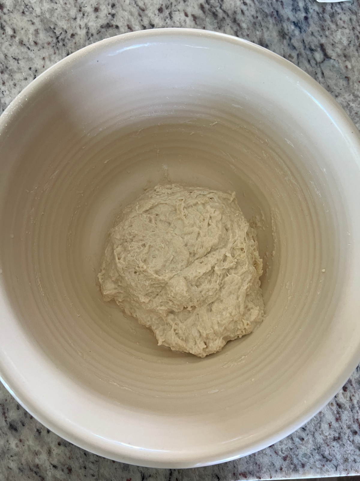 The shaggy just mixed together dough for the sourdough maple pecan bread sits in a ceramic bowl.