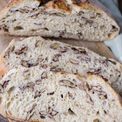 From-scratch sourdough maple pecan bread is shown sliced and sitting on a wooden cutting board.