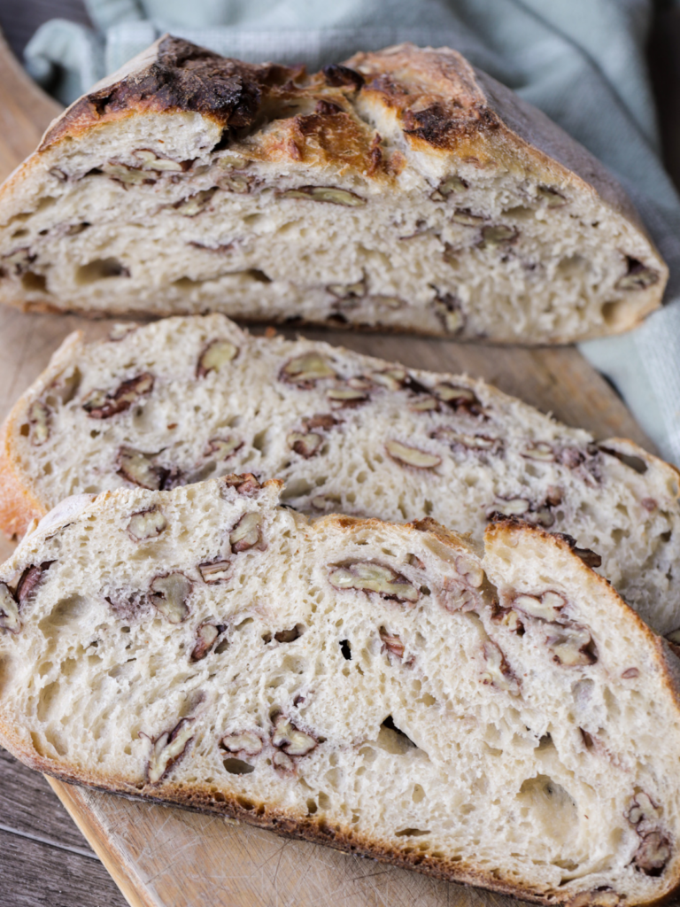 From-scratch sourdough maple pecan bread is shown sliced and sitting on a wooden cutting board.