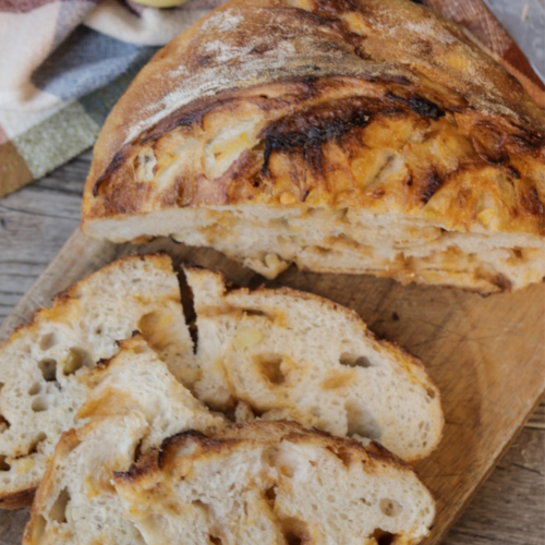 Half a loaf of apple cider butterscotch sourdough bread with several slices of bread resting next to it on a wooden cutting board.
