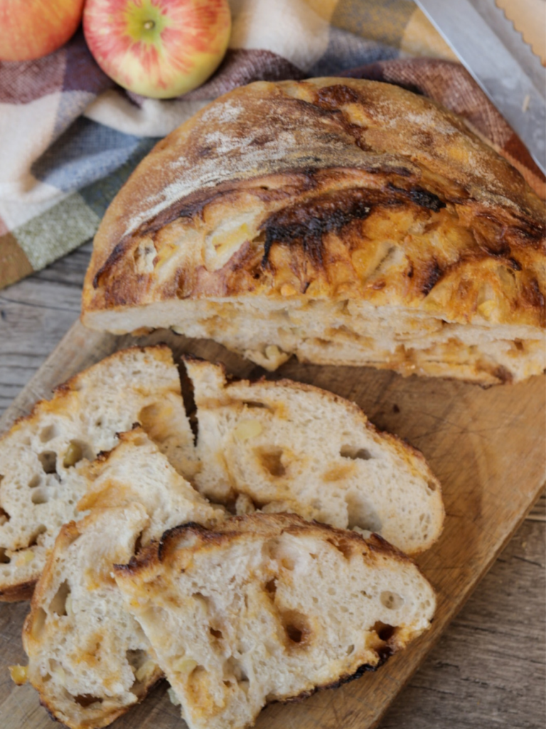 Half a loaf of apple cider butterscotch sourdough bread with several slices of bread resting next to it on a wooden cutting board.