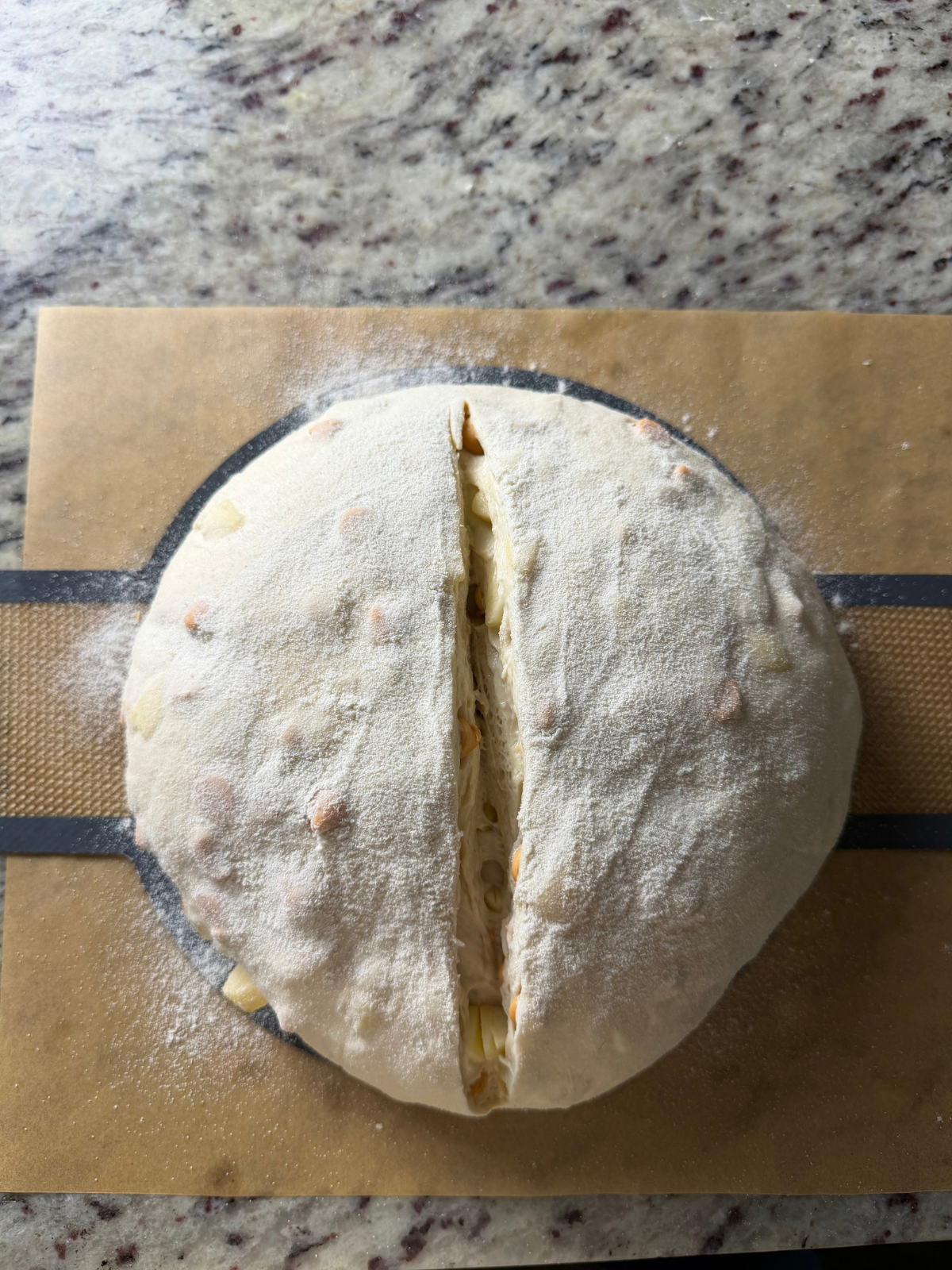 The dough for the sourdough apple cider butterscotch bread is shown on parchment paper and a bread sling after being scored.