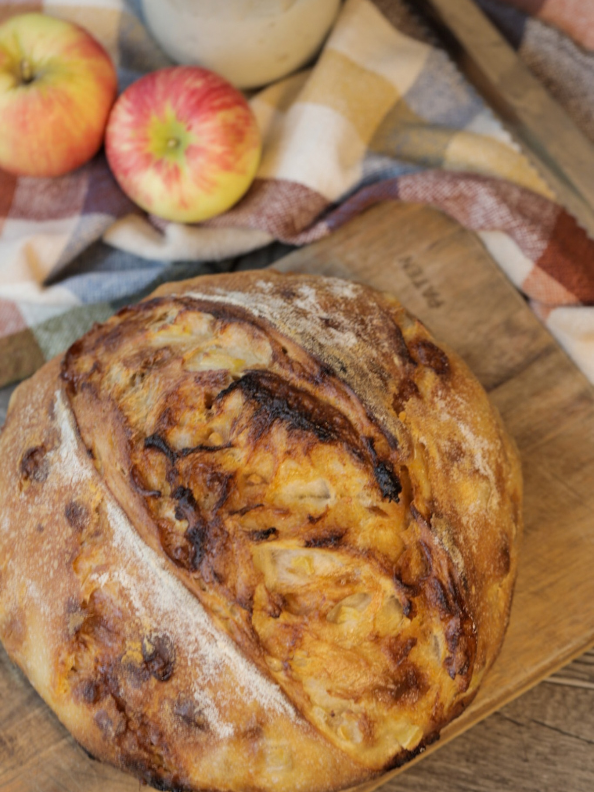 The full and freshly baked loaf of apple cider butterscotch sourdough bread is shown on a wooden cutting board. 