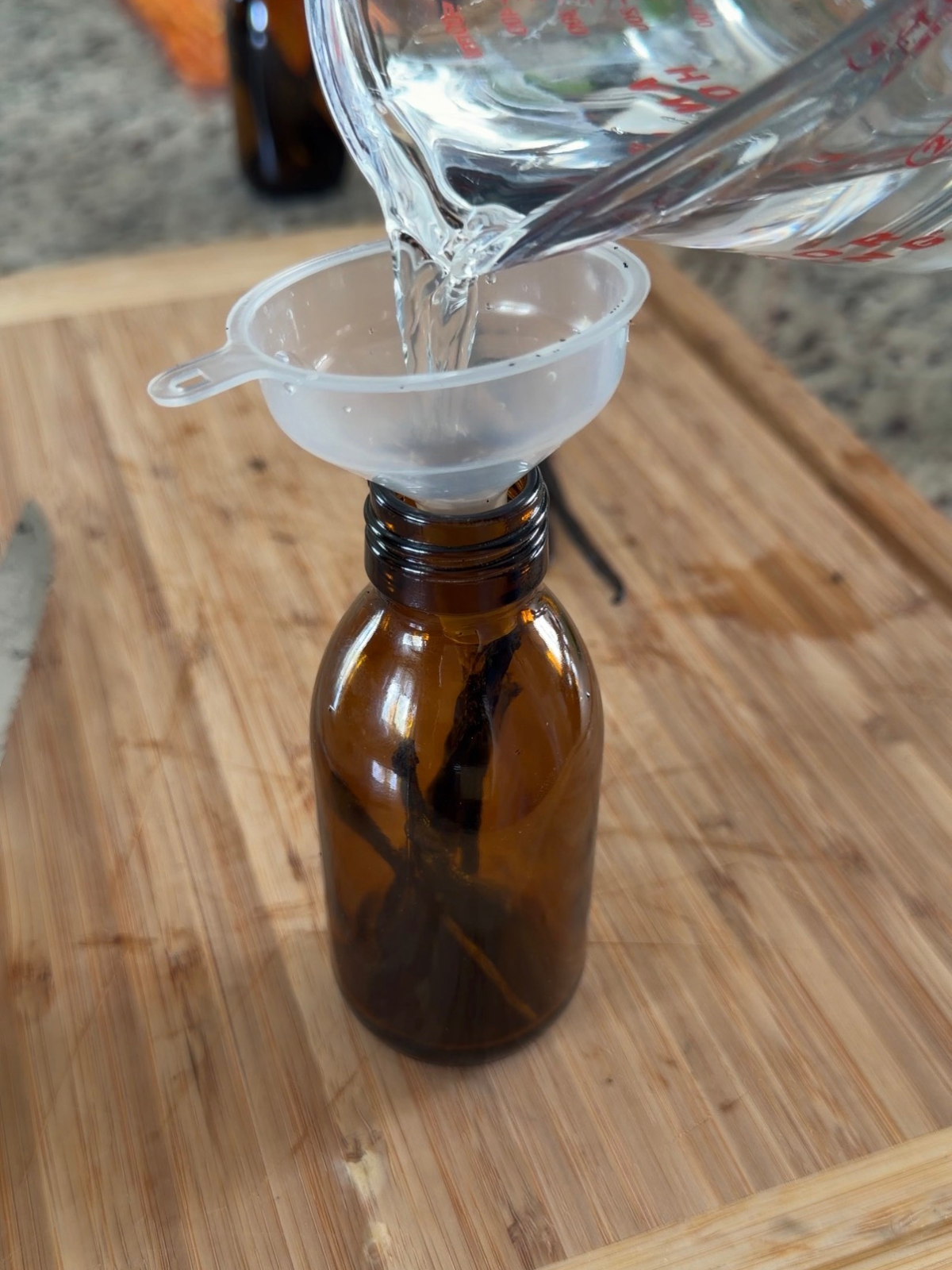 Vodka is being poured through a funnel into the amber glass bottle. 