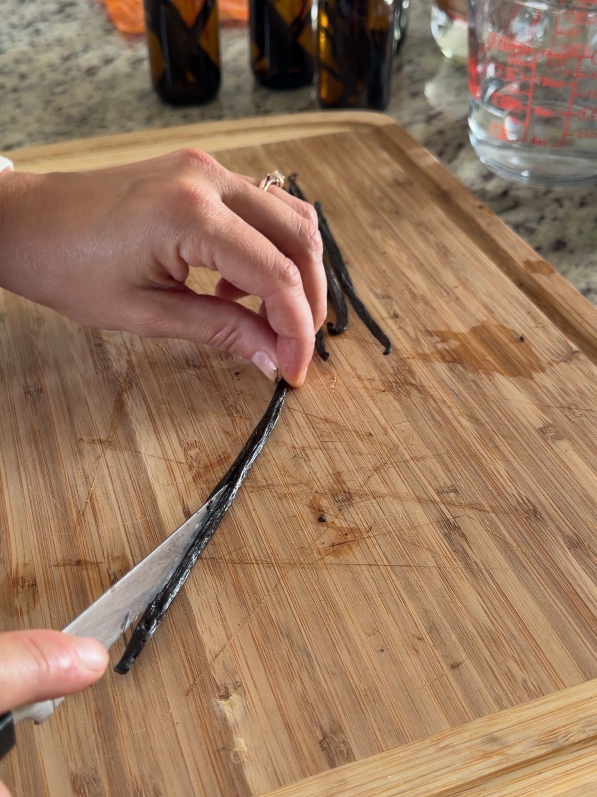 A vanilla bean pod is being sliced right down the center on a wooden cutting board.