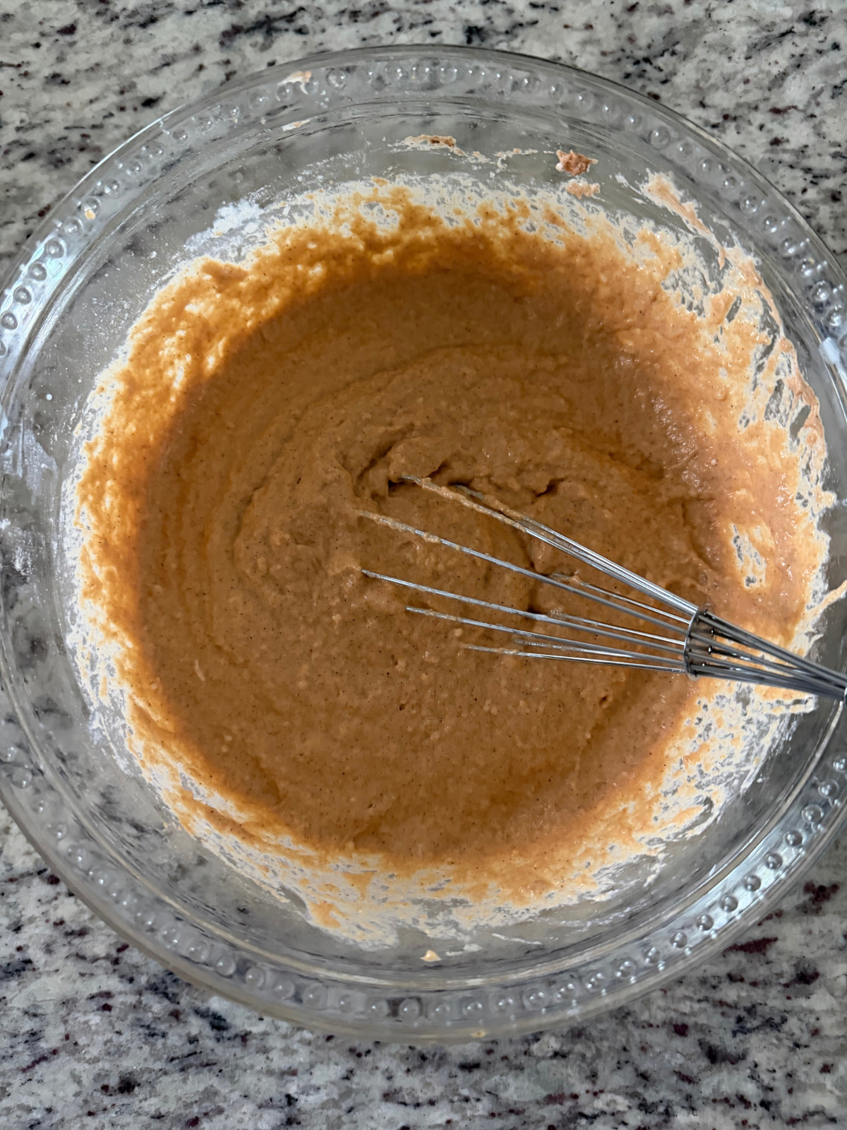 The sourdough pumpkin pancake batter sits in a glass mixing bowl with a whisk in it. It is ready to be cooked with after an overnight ferment.