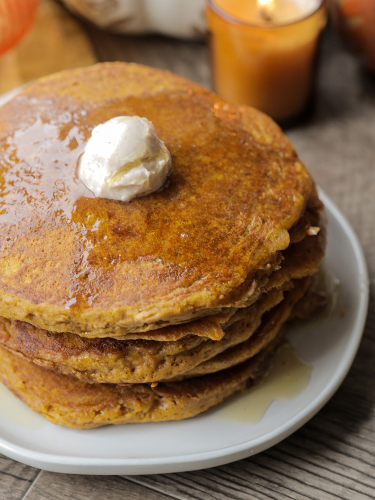A closeup of five soft and fluffy sourdough pumpkin pancakes with maple syrup and cinnamon butter is shown.