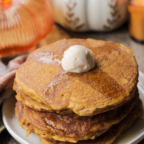 Soft and fluffy sourdough pumpkin pancakes are shown on a plate with cinnamon butter and maple syrup.
