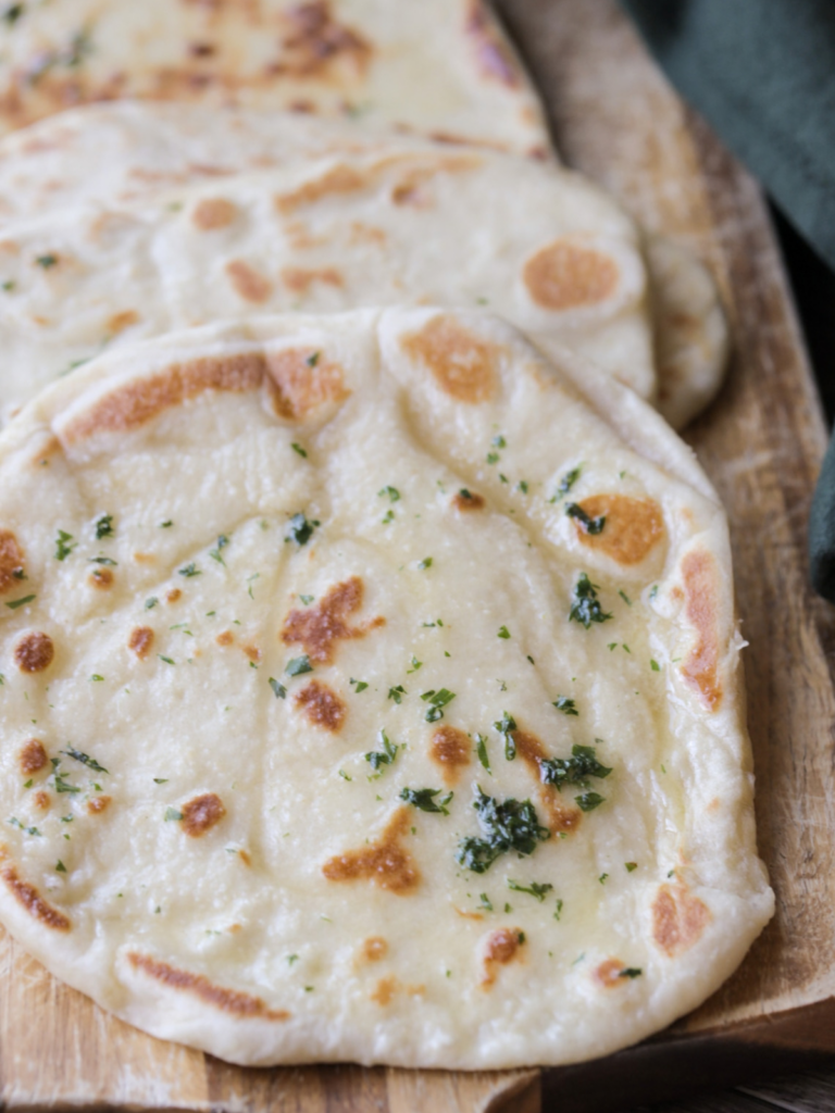 A closeup is shown of this from-scratch sourdough discard naan that is brushed with a cilantro garlic butter.