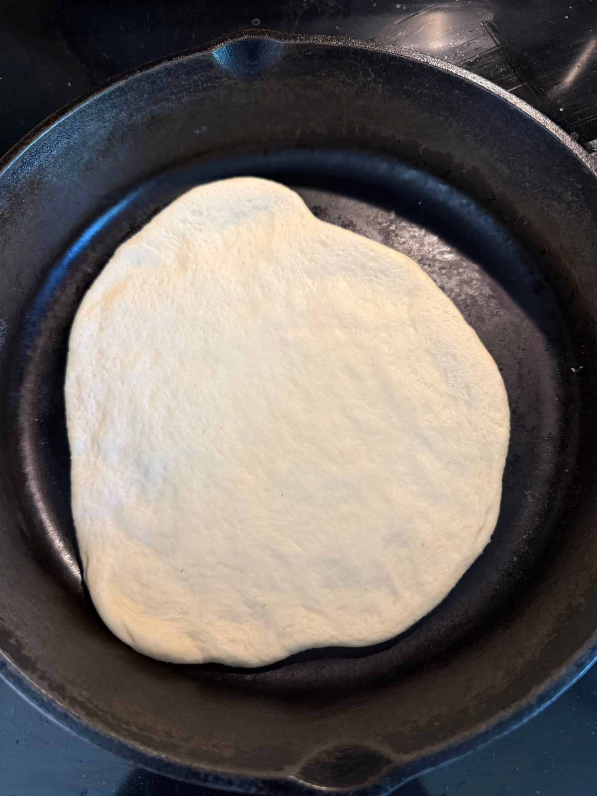 The sourdough naan cooks on a cast iron skillet.