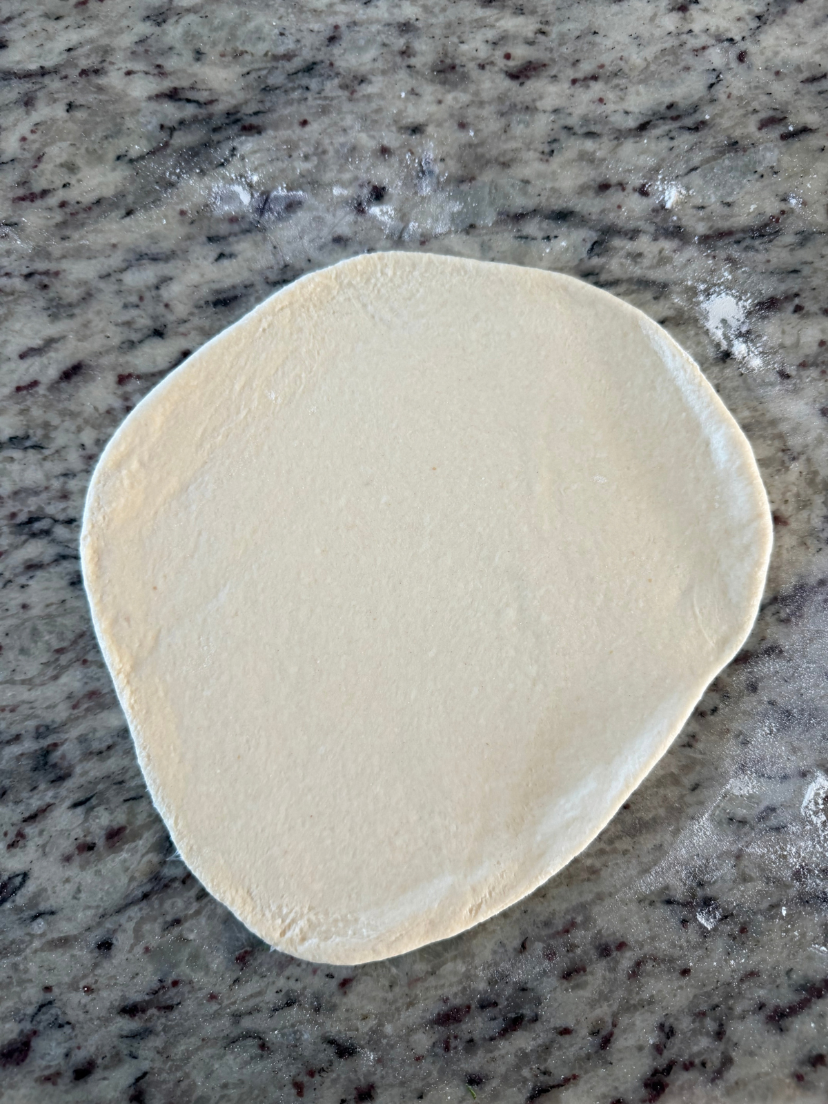 The sourdough discard naan dough sits on the counter after being rolled out. 