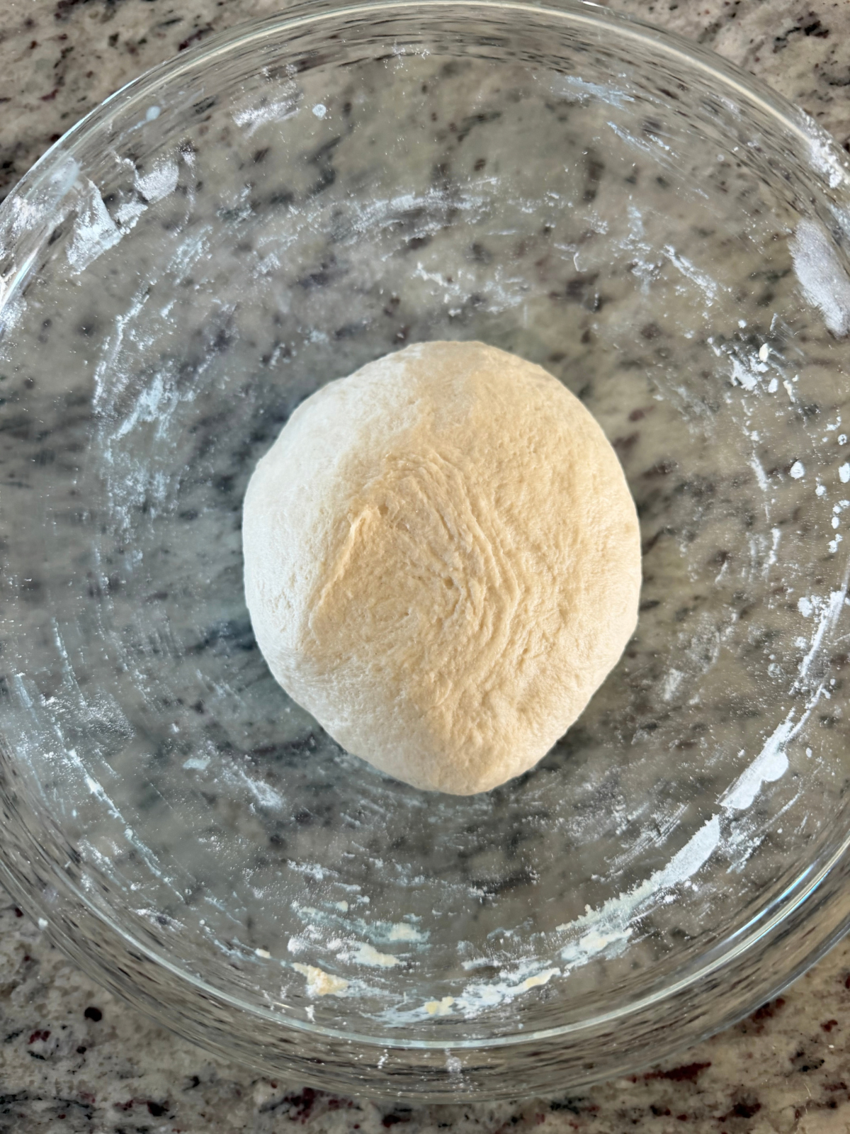 The sourdough discard naan has been kneaded into a round ball and sits in the glass mixing bowl.