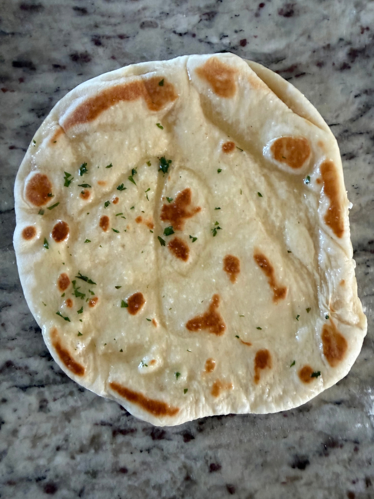 The sourdough discard naan has been brushed with a cilantro garlic butter and is ready to be enjoyed.