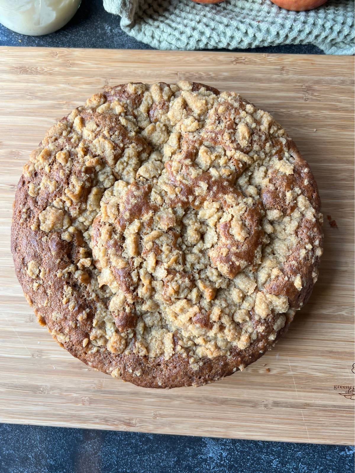 The freshly baked sourdough discard apple coffee cake sits on a wooden cutting board. It is cooling and then will be topped with a simple vanilla icing.