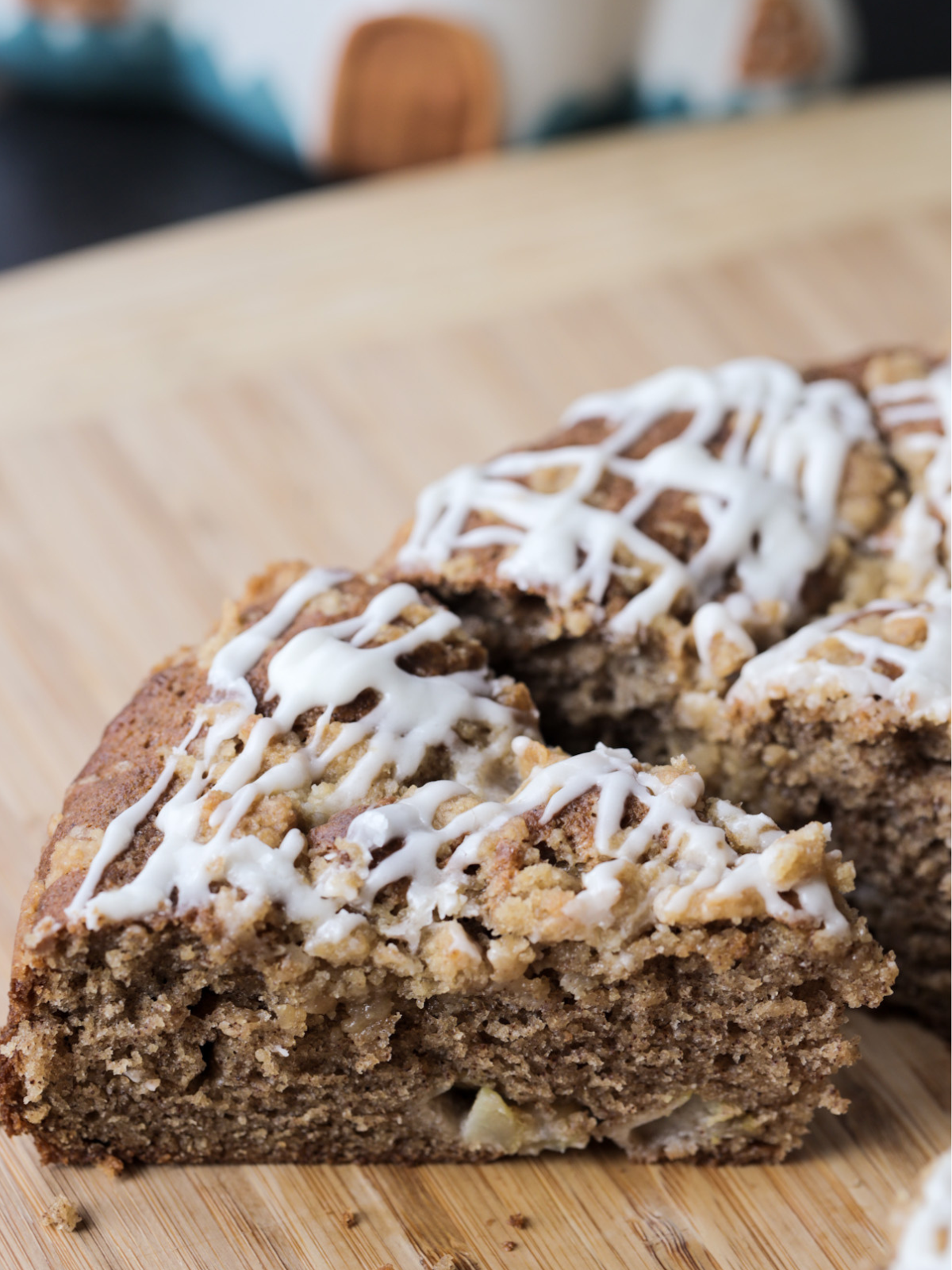 A couple sourdough discard apple streusel coffee cake slices sit on the wooden cutting board with vanilla icing drizzled over it.