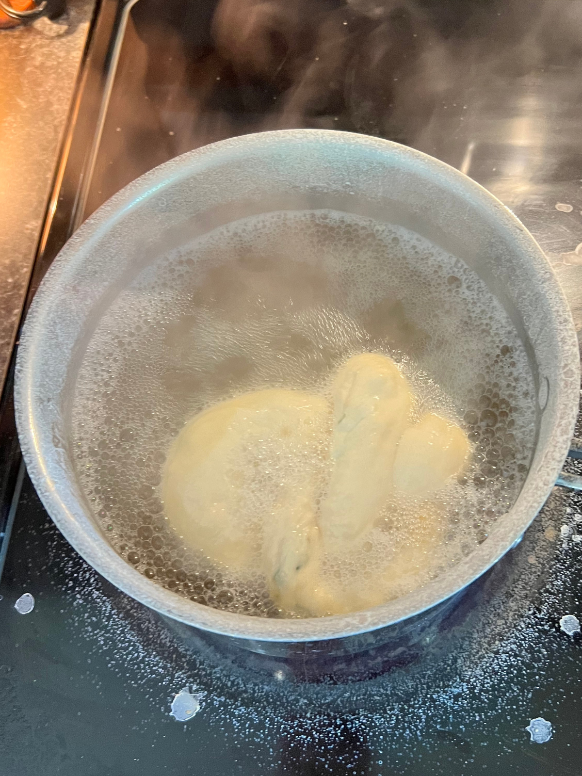 A sourdough pretzel is shown boiling in a baking soda bath.