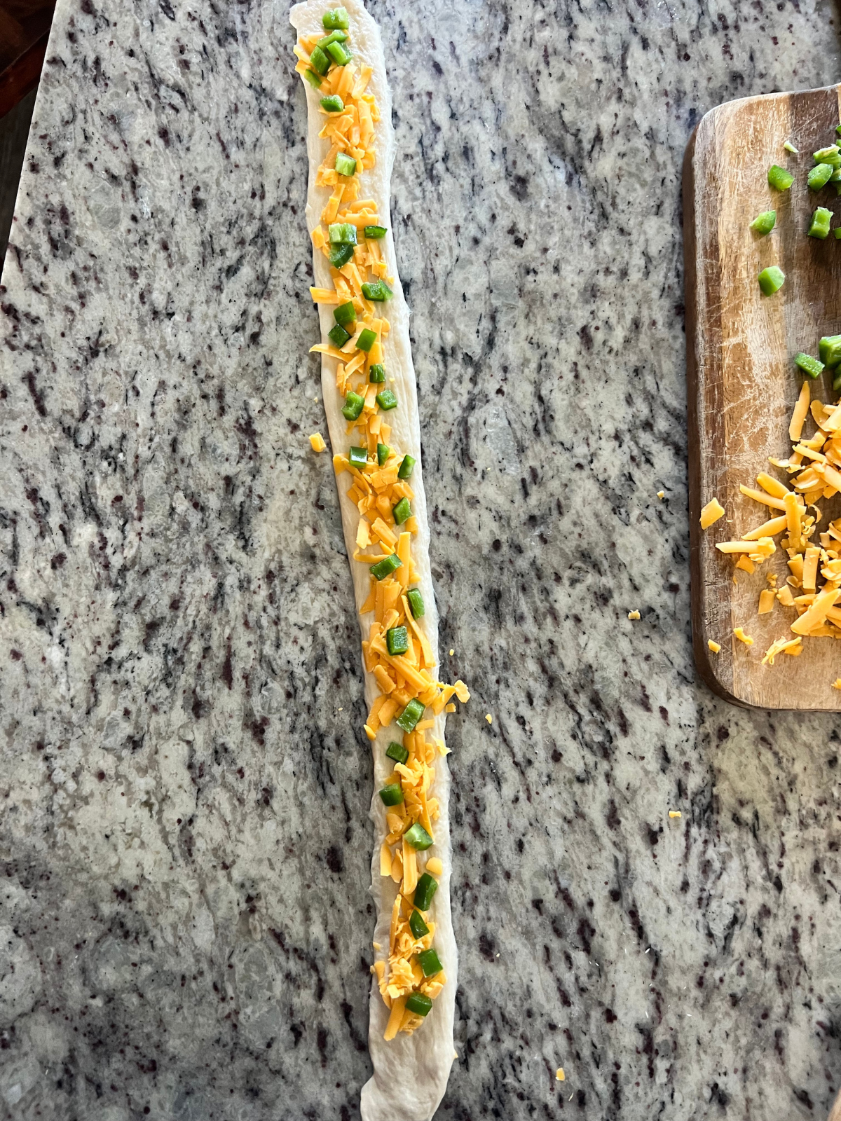 A sourdough pretzel dough rope is shown flattened out with the sharp cheddar cheese and diced jalapenos.