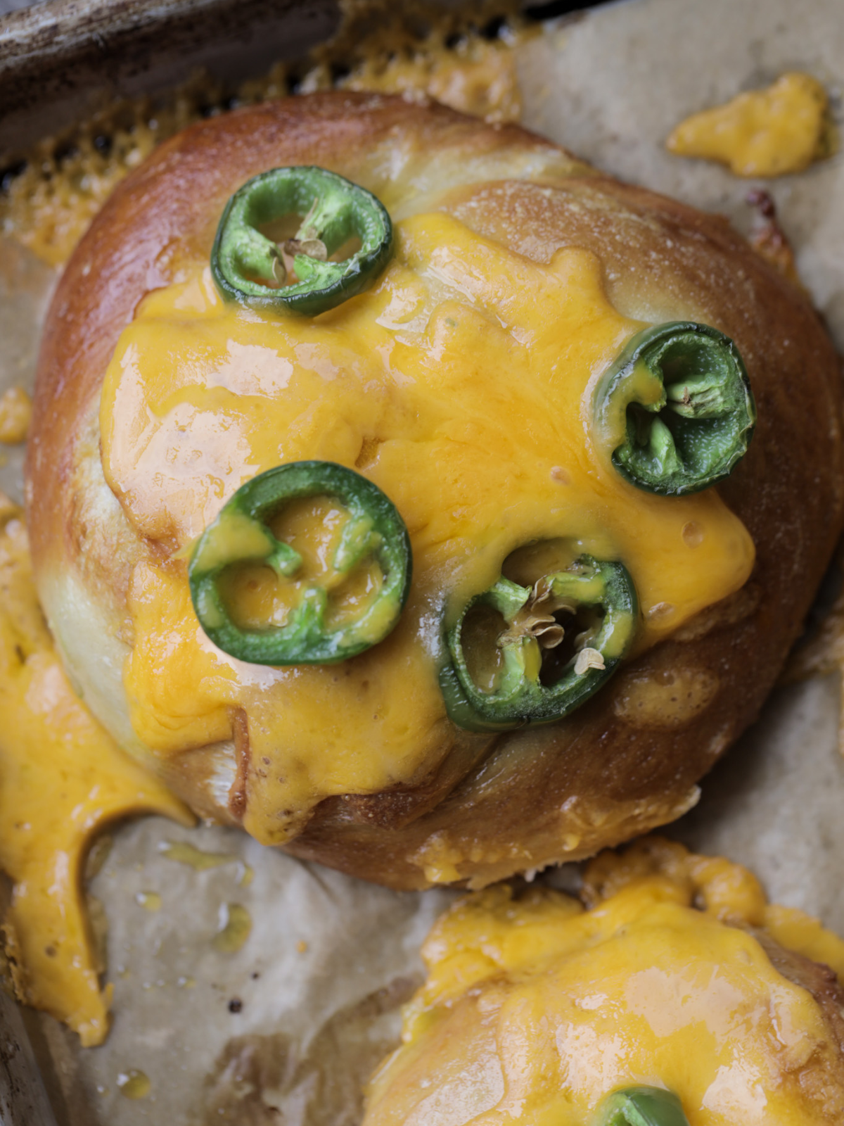 A golden brown 100% sourdough pretzel is shown with gooey sharp cheddar cheese and sliced jalapenos. It's also stuffed with more cheese and jalapenos.