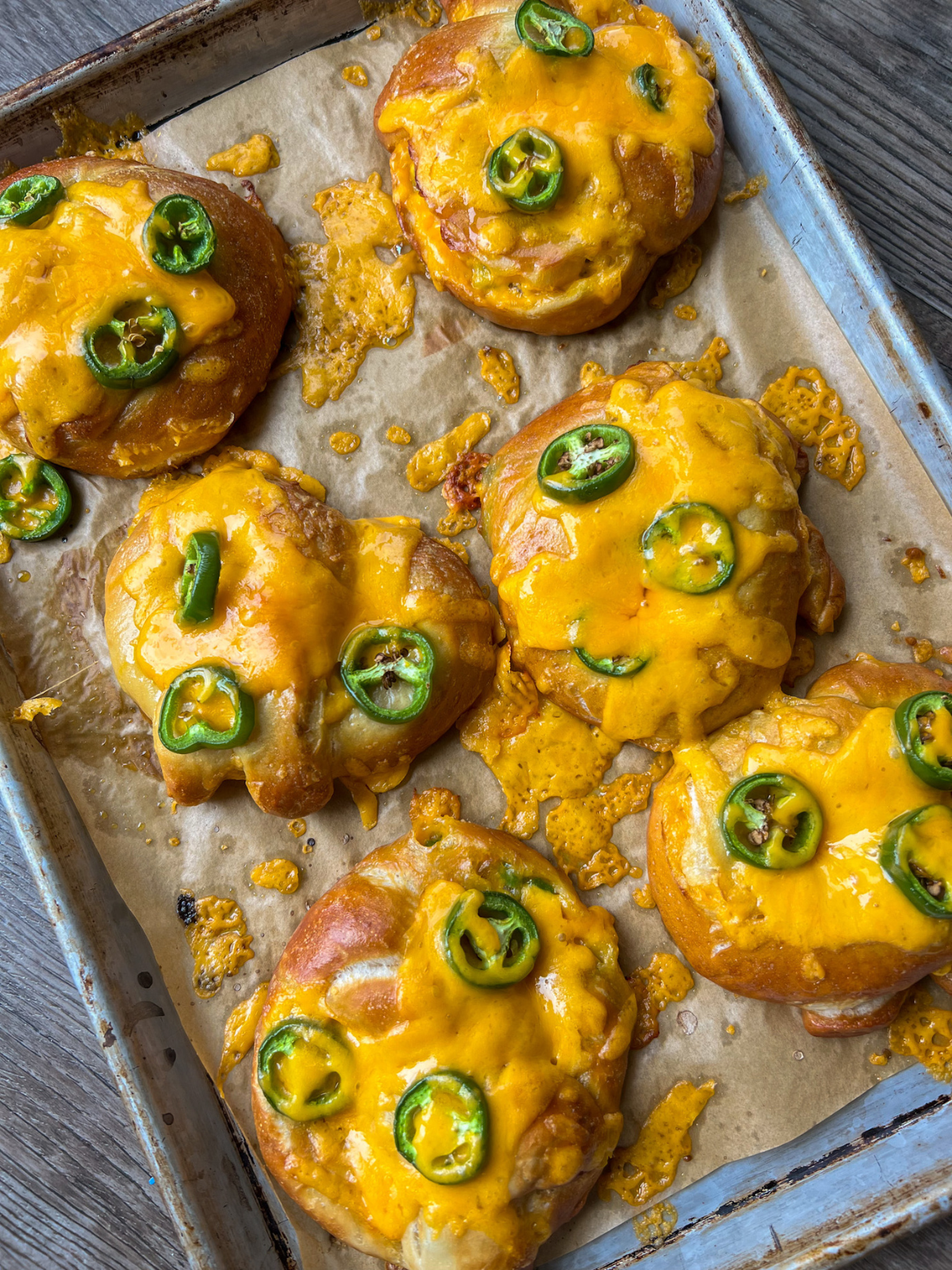 The freshly baked sourdough soft pretzels with jalapenos and cheddar cheese are shown on a parchment-lined baking sheet.