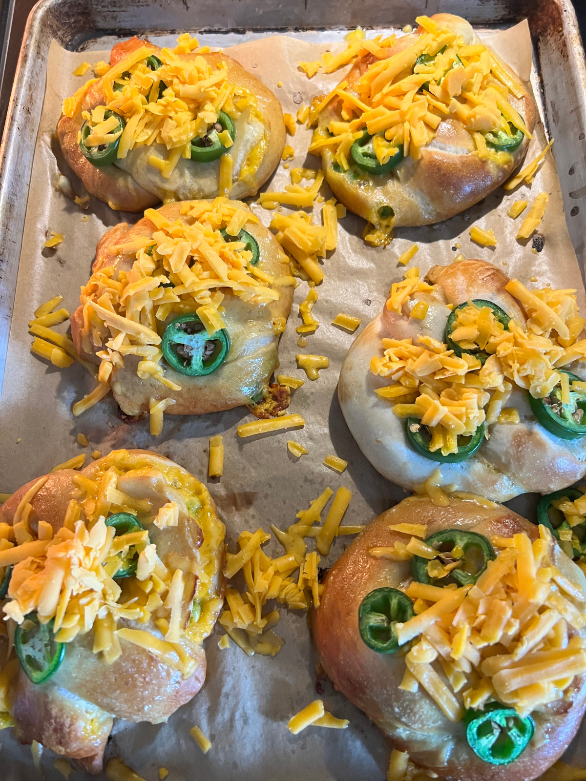 The mostly baked sourdough jalapeno and cheddar pretzels are shown with freshly shredded sharp cheddar cheese on top. This cheese will melt after going in the oven for another five minutes.