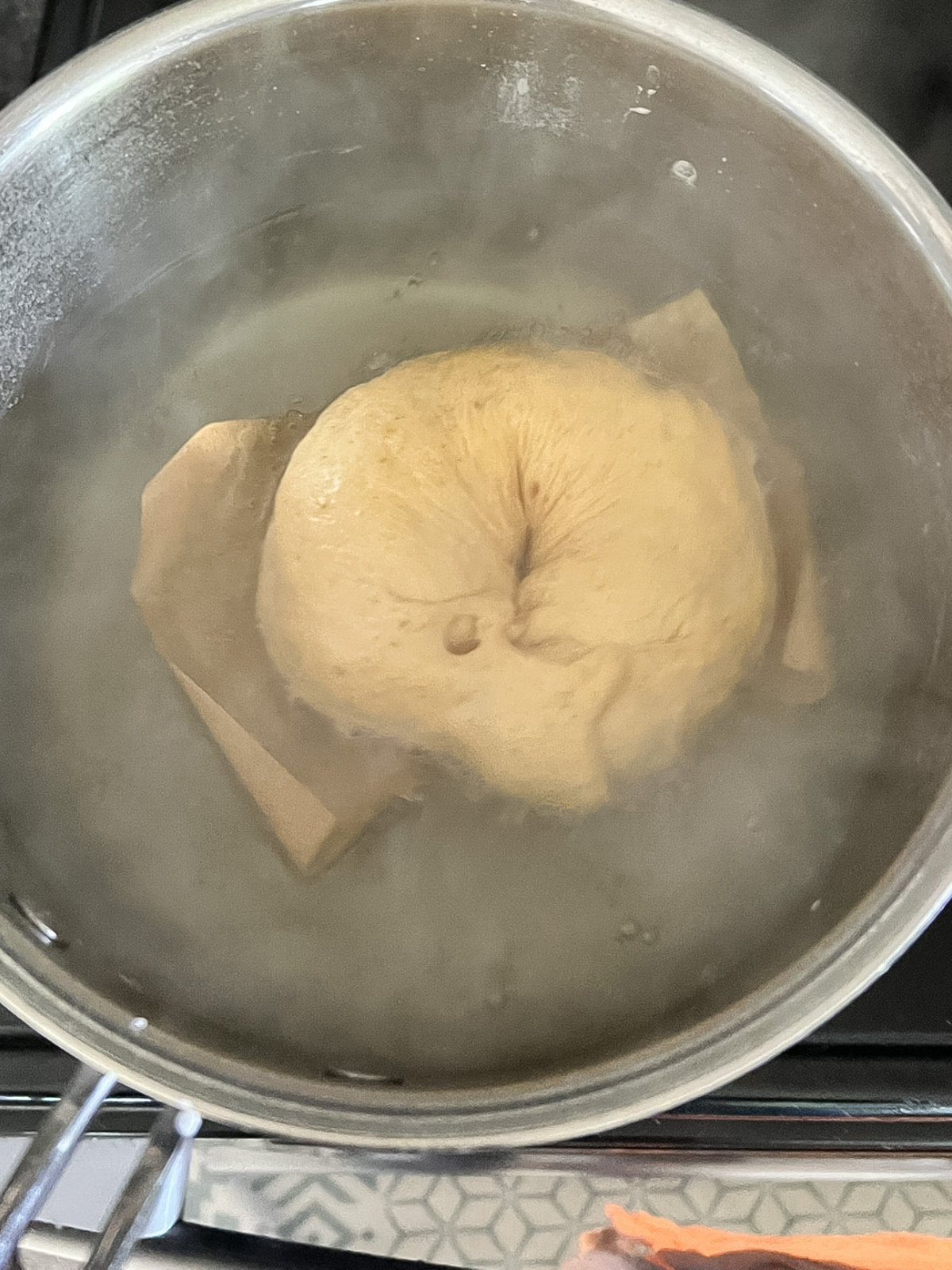 A sourdough pumpkin cinnamon swirl bagel is shown boiling in a baking soda bath. 