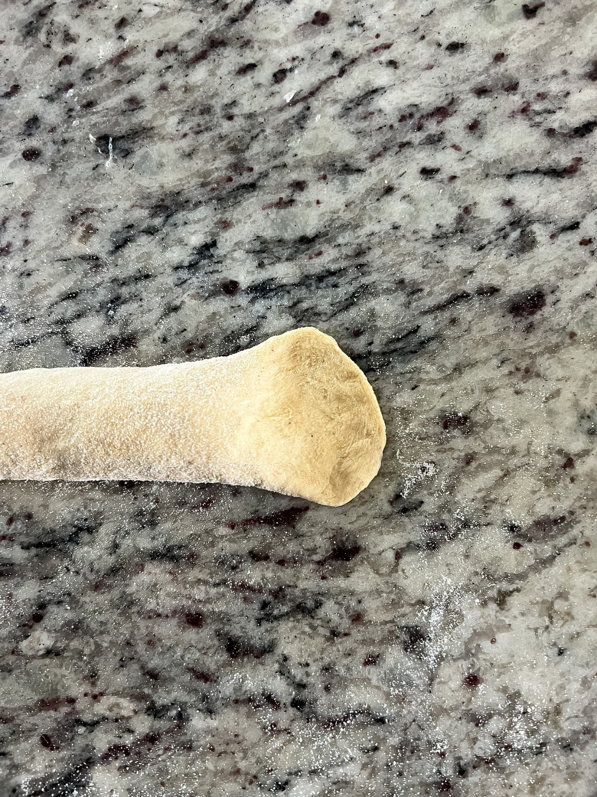 The end of one side of the dough rope has been pressed down to easily wrap it around the other end of the rope to form the bagel shape.