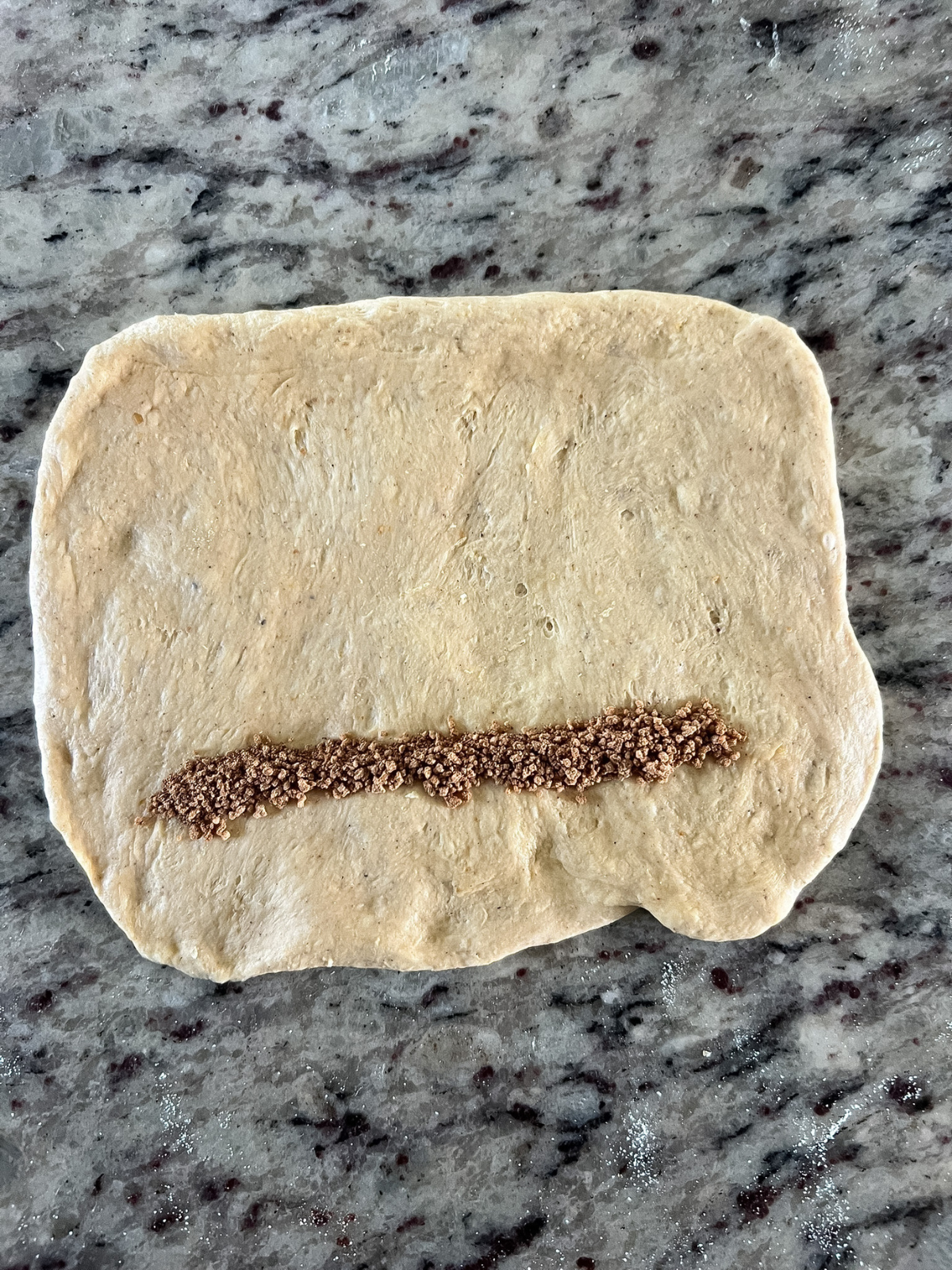 A line of the cinnamon brown sugar flour mixture has been spread across the rectangle of dough.