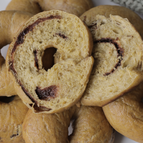 A closeup of a sourdough pumpkin cinnamon swirl bagel is shown with several other bagels in the background.