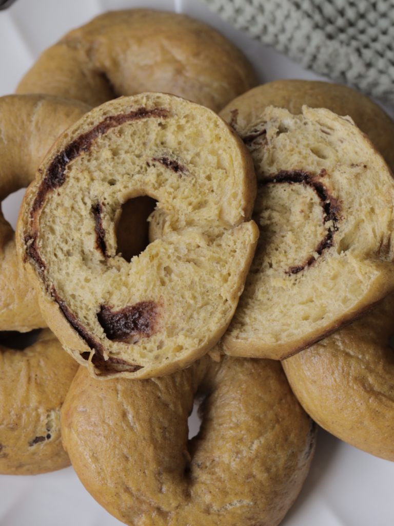 A closeup of a sourdough pumpkin cinnamon swirl bagel is shown with several other bagels in the background.