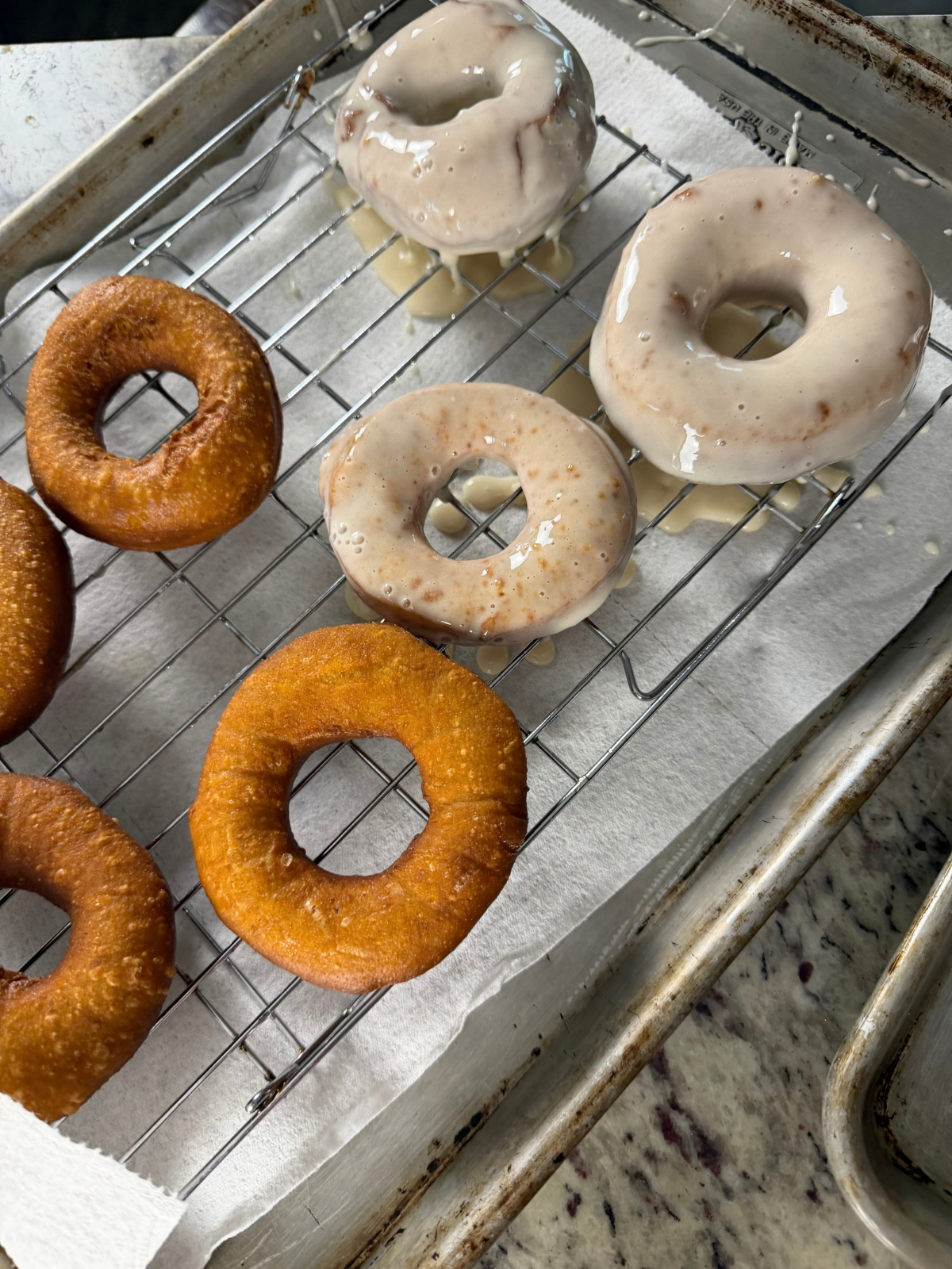 Several sourdough pumpkin donuts are shown on a wire rack. A few of them have already been glazed with the maple glaze.
