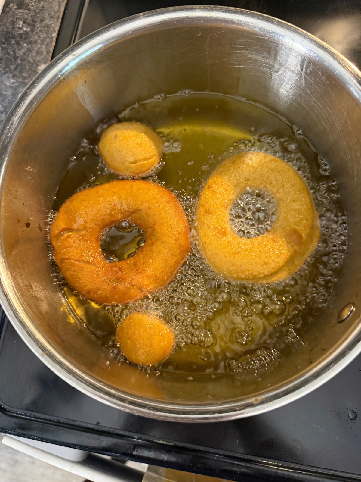 Several sourdough pumpkin donuts and donut holes are shown frying in the oil on the stovetop.