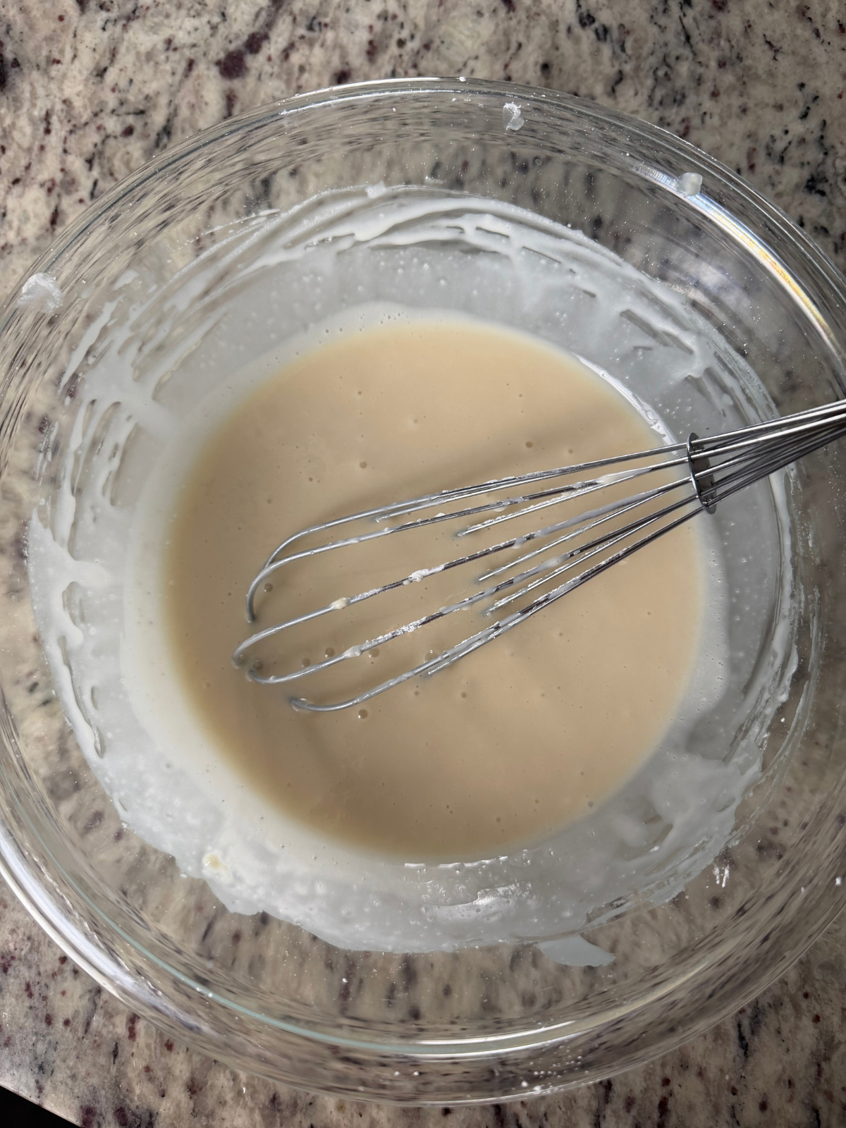Maple glaze sits in a glass mixing bowl with a whisk in it.