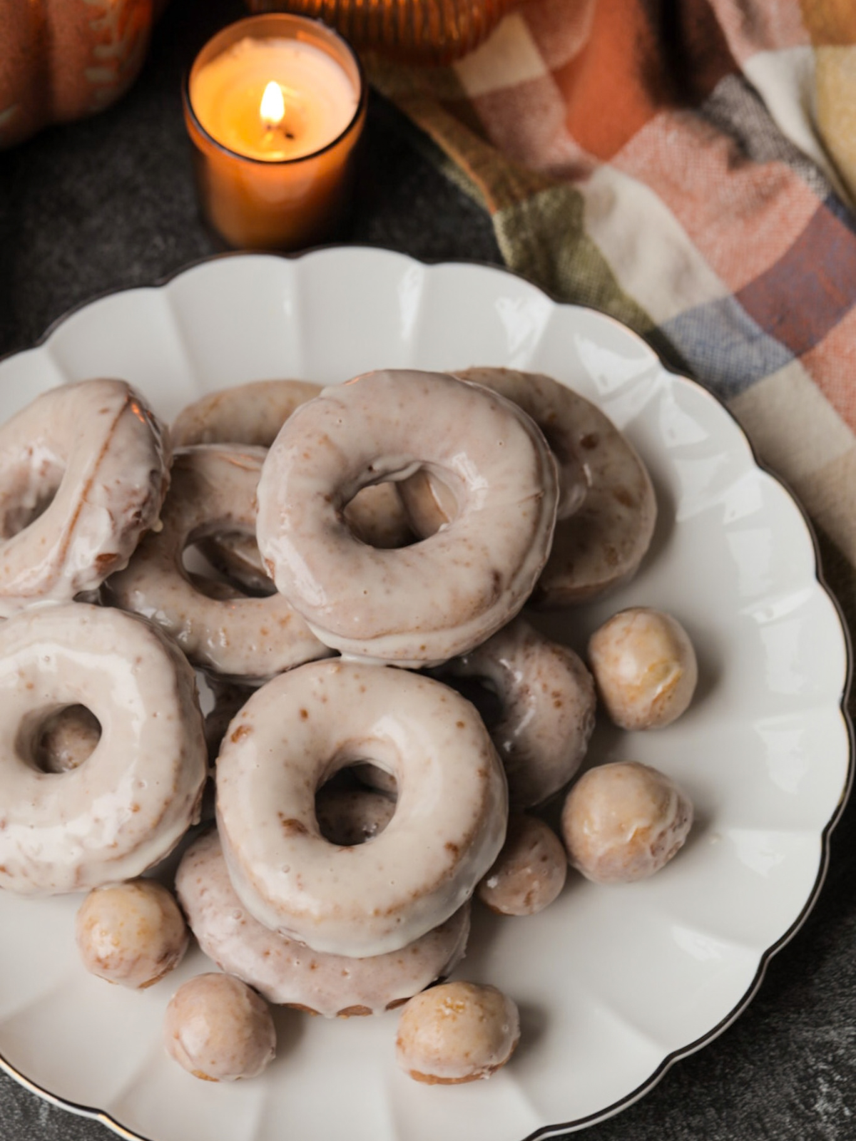 Twelve sourdough pumpkin donuts with maple glaze are shown on a platter. A candle is lit in the background.