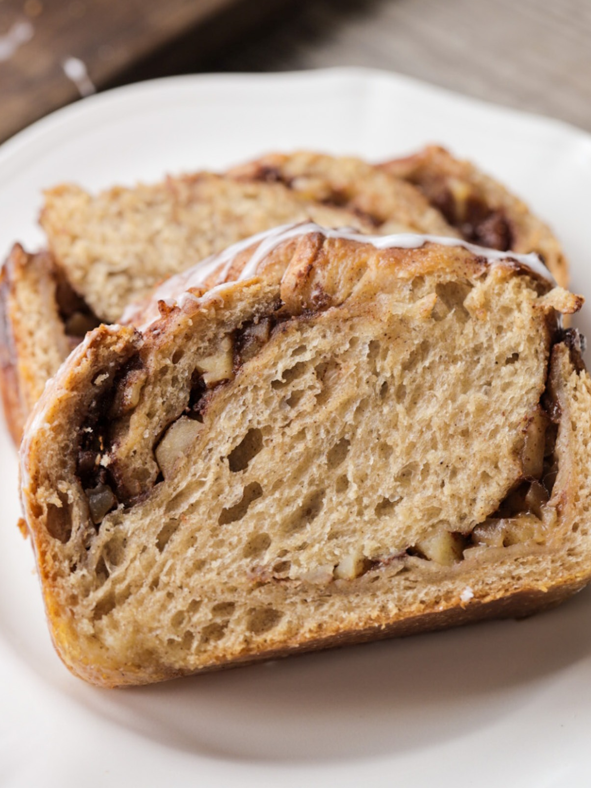 Ribbons of apples and cinnamon swirl are shown throughout in a closeup of the sourdough apple-filled babka slice of bread. 