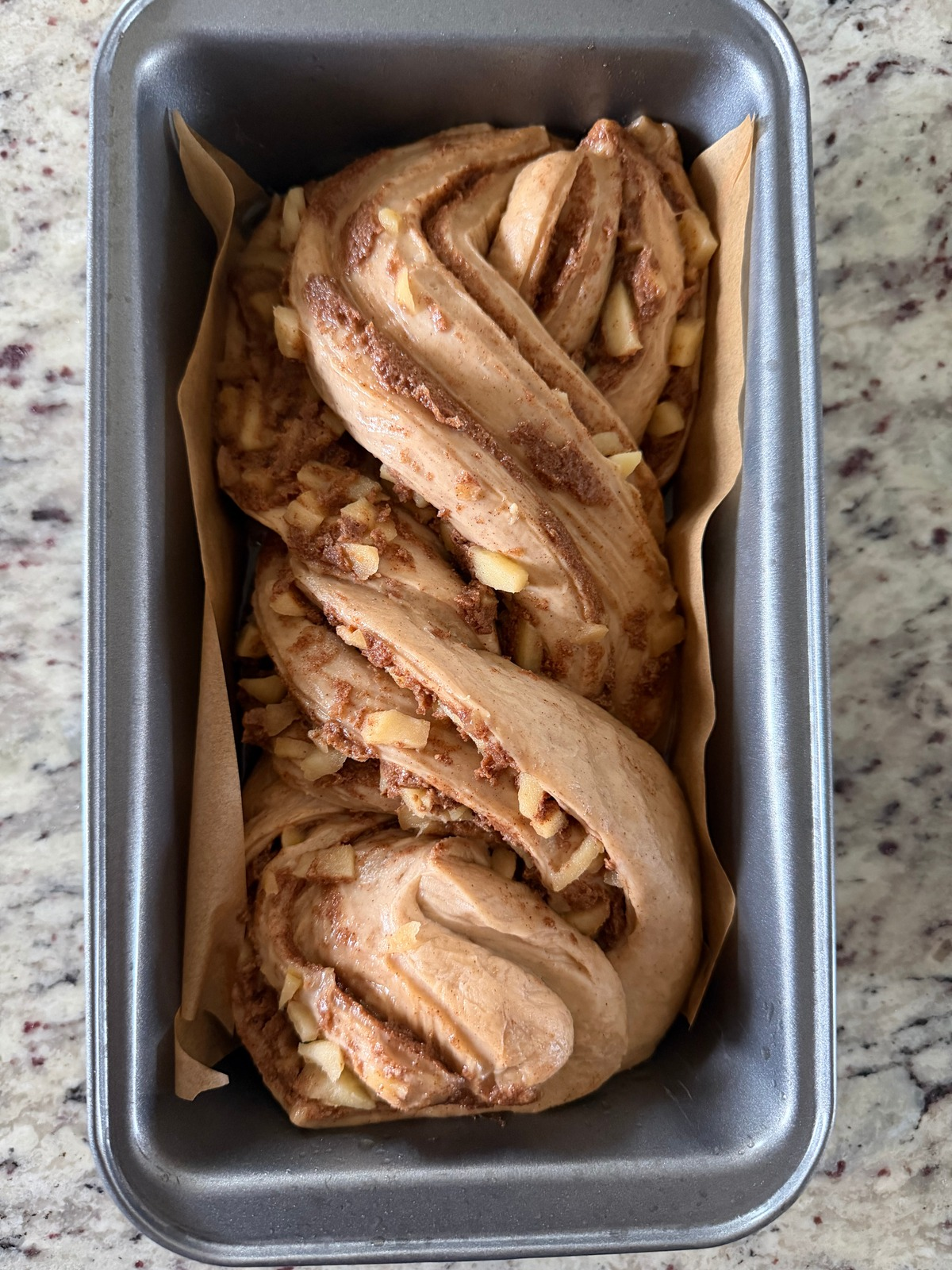 The apple sourdough babka dough is shown in a parchment paper lined 9x5 loaf pan after its second rise.
