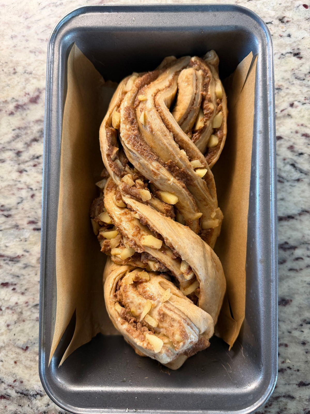 The apple sourdough babka dough is shown in a parchment paper lined 9x5 loaf pan before its second rise.