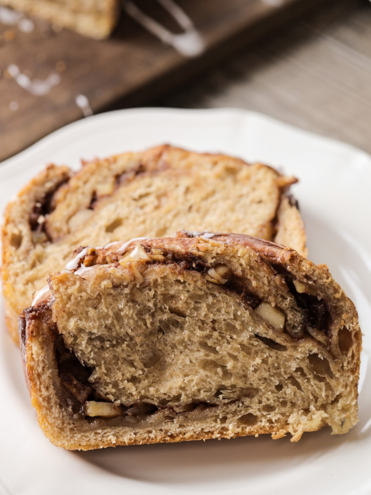 A close up of a couple slices of sourdough apple-filled babka is shown. You can see the ribbons of cinnamon swirl and the diced apples throughout.